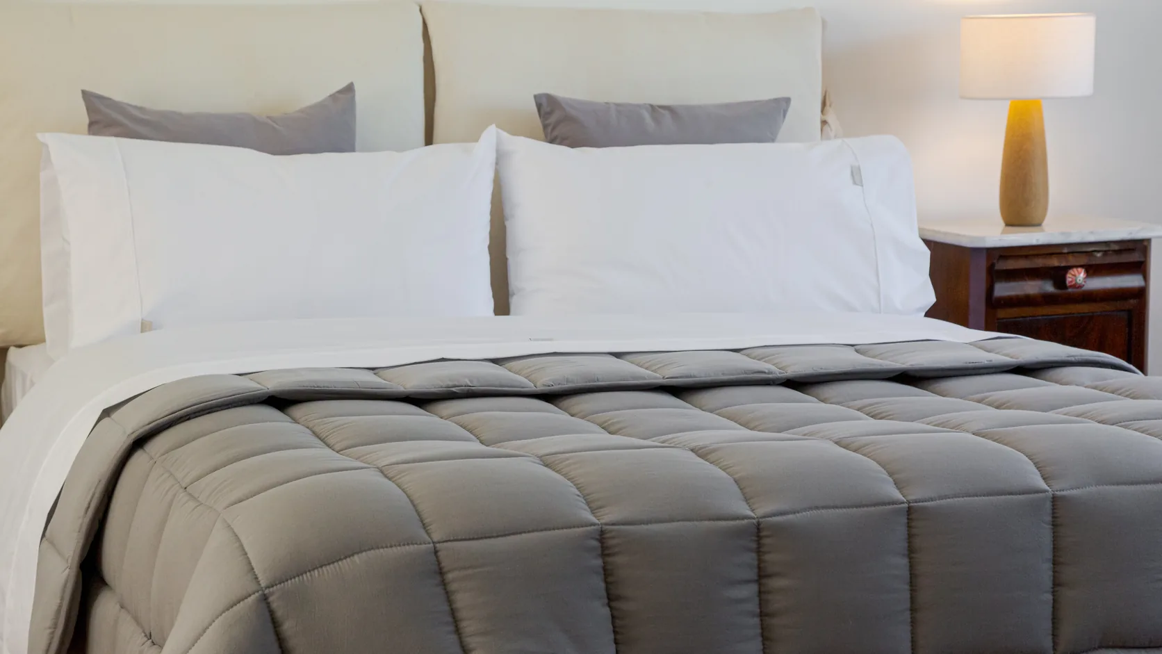 Cama tendida con acolchado Brescia en gris y almohadas blancas