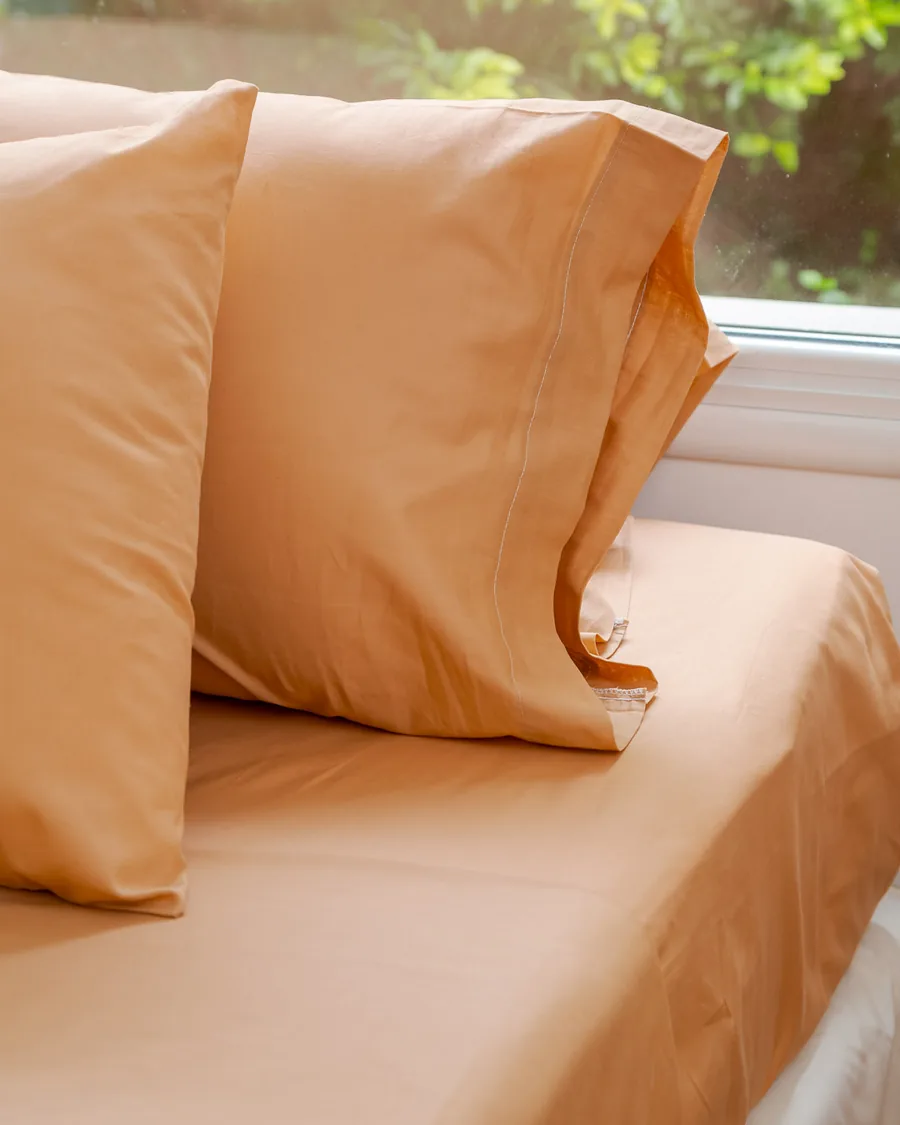 Fundas y sábanas Brescia en tono naranja sobre la cama, junto a la ventana