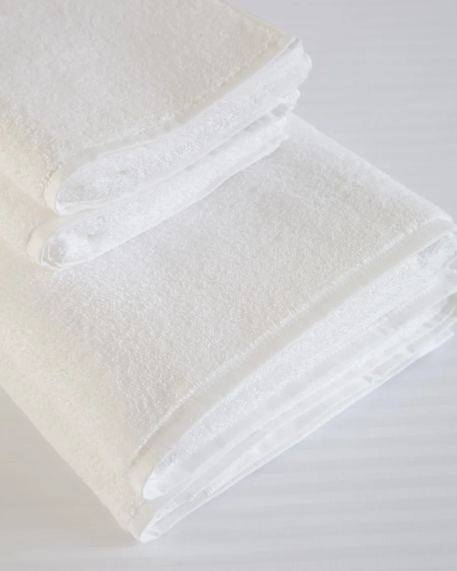 Toallas y toallones blancos Brescia apilados sobre la cama